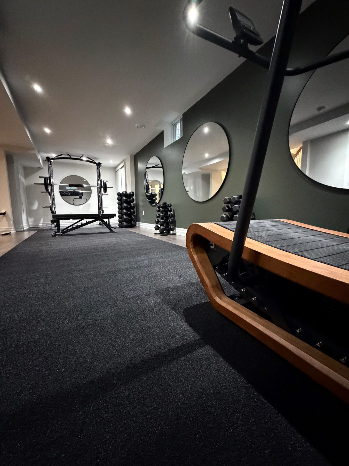 Curved treadmill, dumbbell racks and circular mirrors along the green feature wall of Mandy's studio